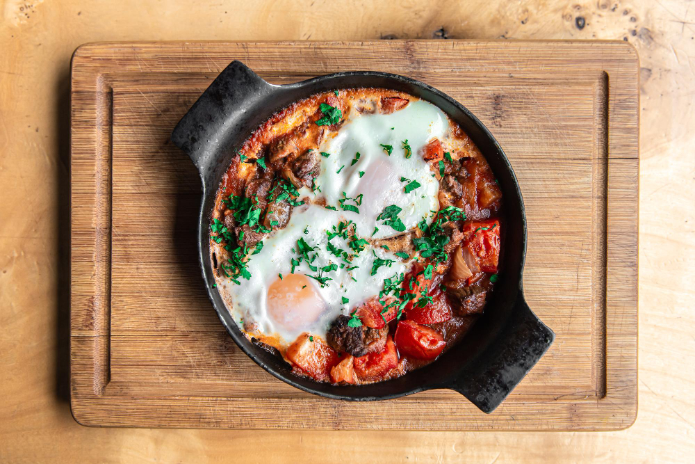 A bowl of shakshuka served on wooden cutting board.